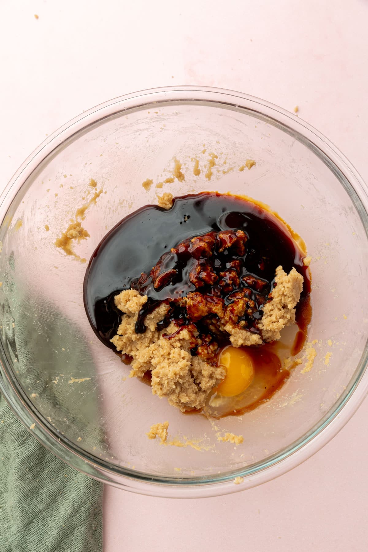 A glass mixing bowl with butter, brown sugar, egg and molasses in it before mixing together.