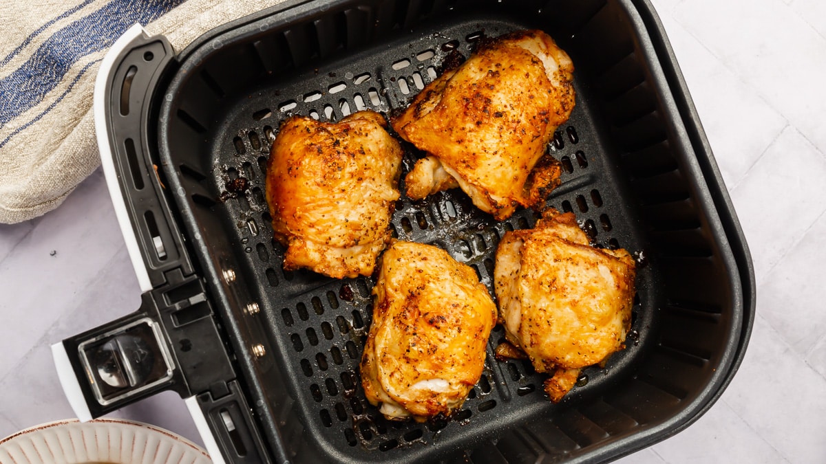 Four crispy bone-in chicken thighs in an air fryer basket after cooking.