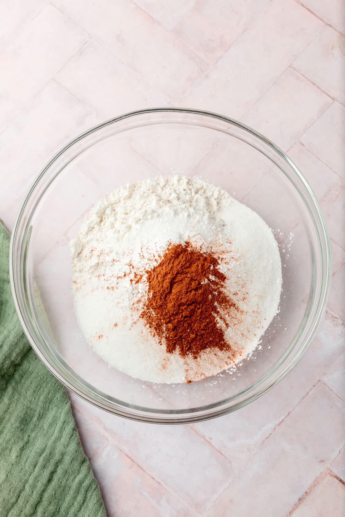 A glass mixing bowl with gluten-free flour blend, cinnamon, salt, baking powder, and baking soda.