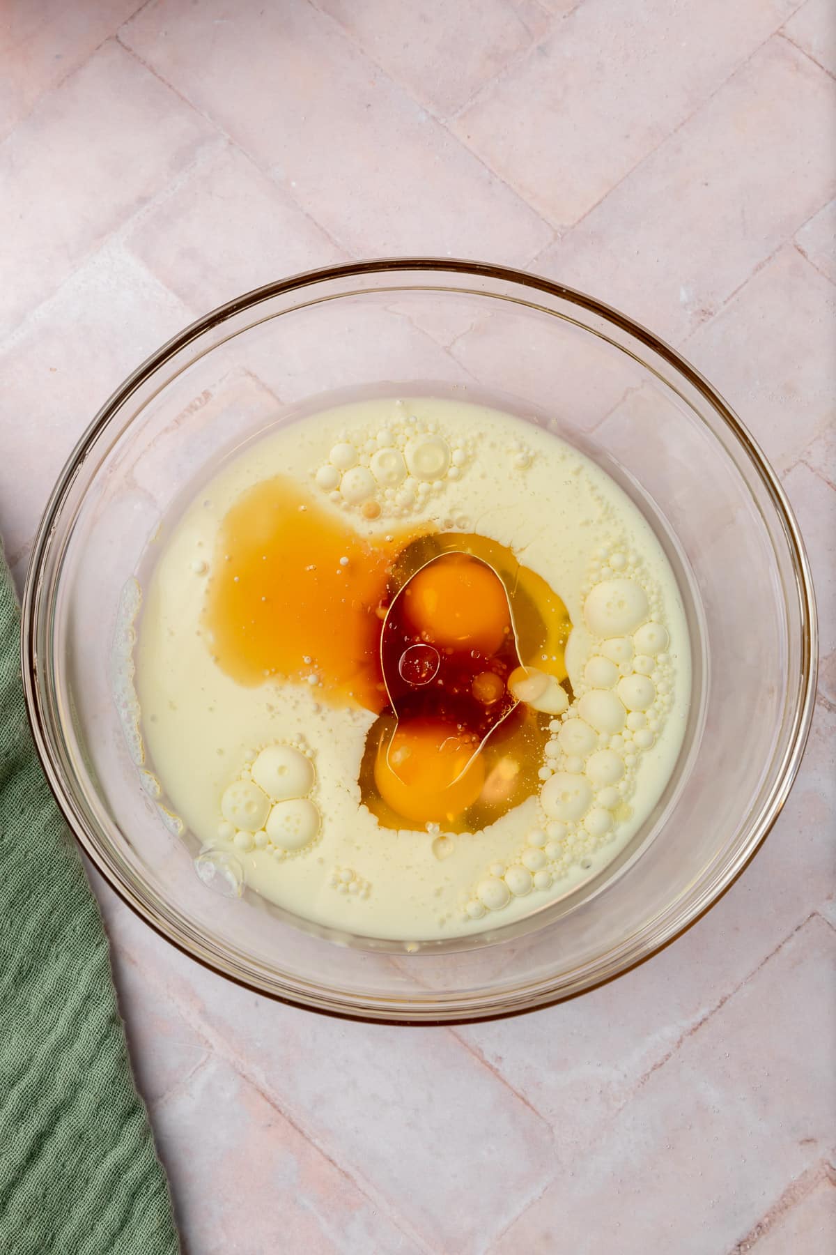 A glass mixing bowl with milk, vegetable oil, eggs, and vanilla in it.