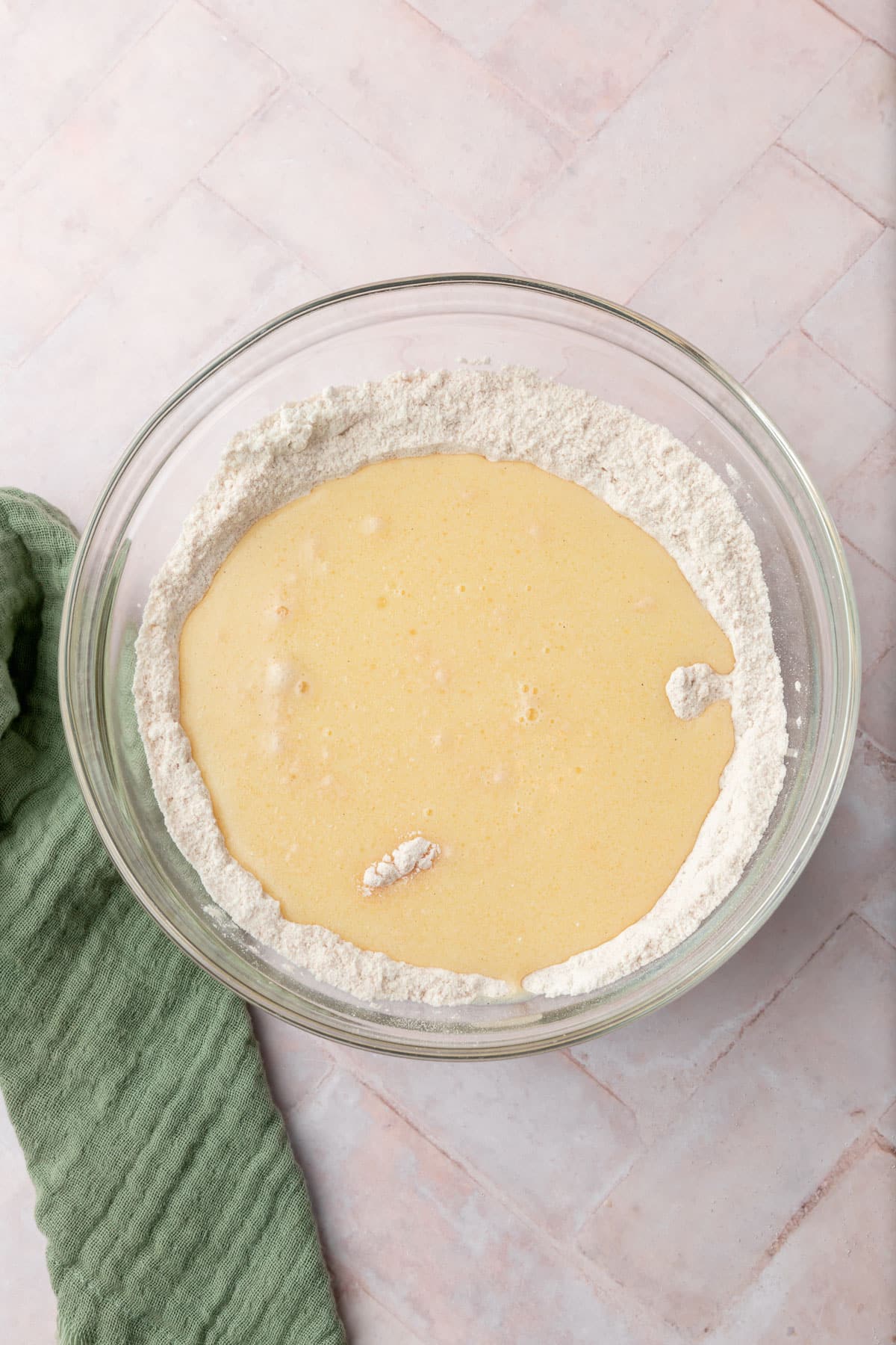 Wet ingredients added to a gluten-free flour mixture in a glass bowl.