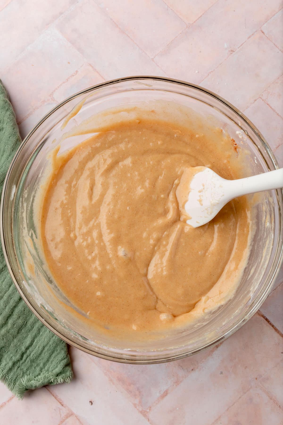 A glass mixing bowl with gluten-free muffin batter in it with a pink spatula.