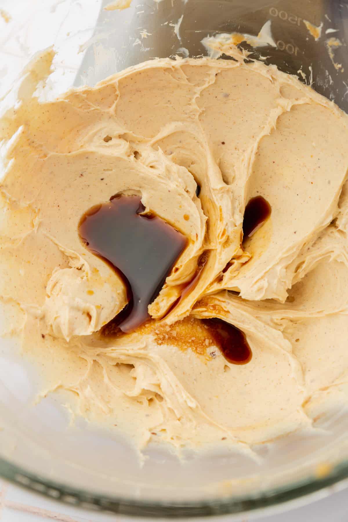 A glass mixing bowl with browned butter and cream cheese mixture topped with vanilla extract.