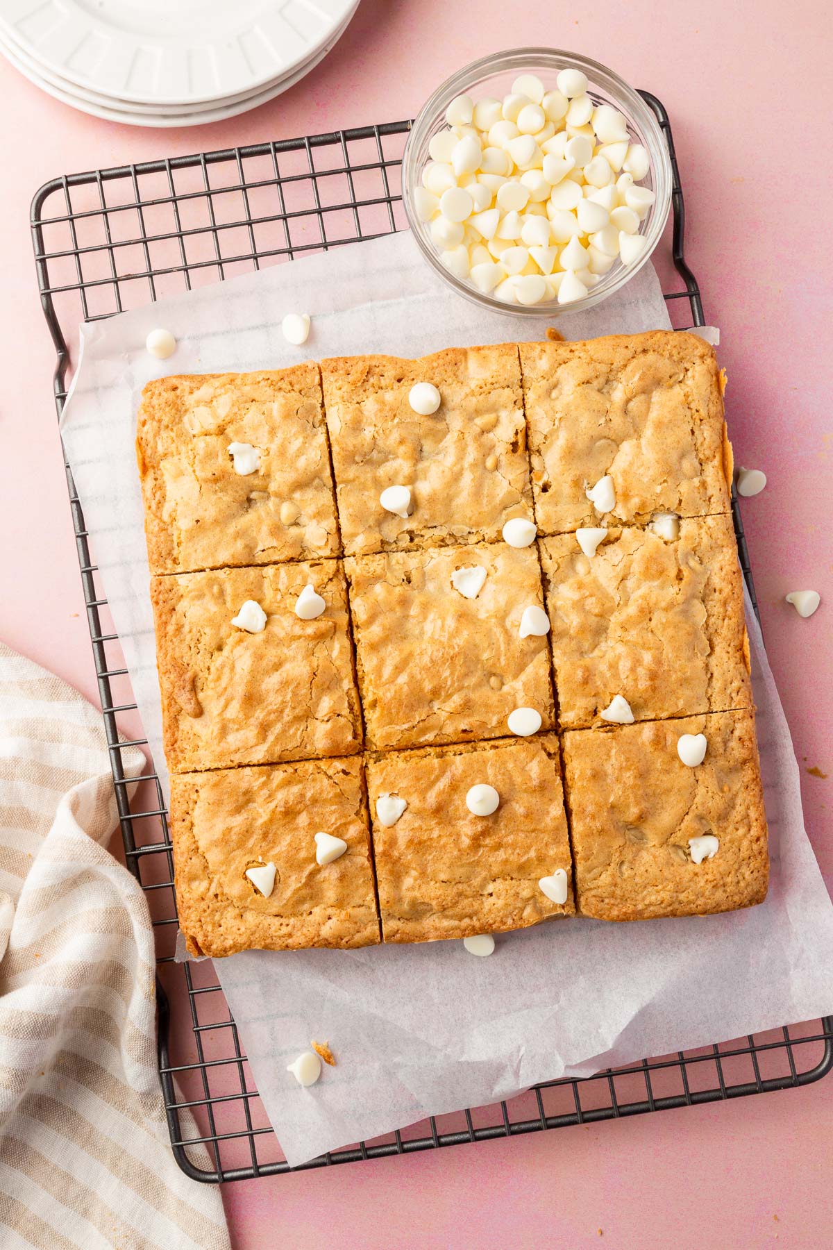 Gluten-free blondies topped with chocolate chips cut into 9 equal squares on a wire cooling rack with parchment paper.