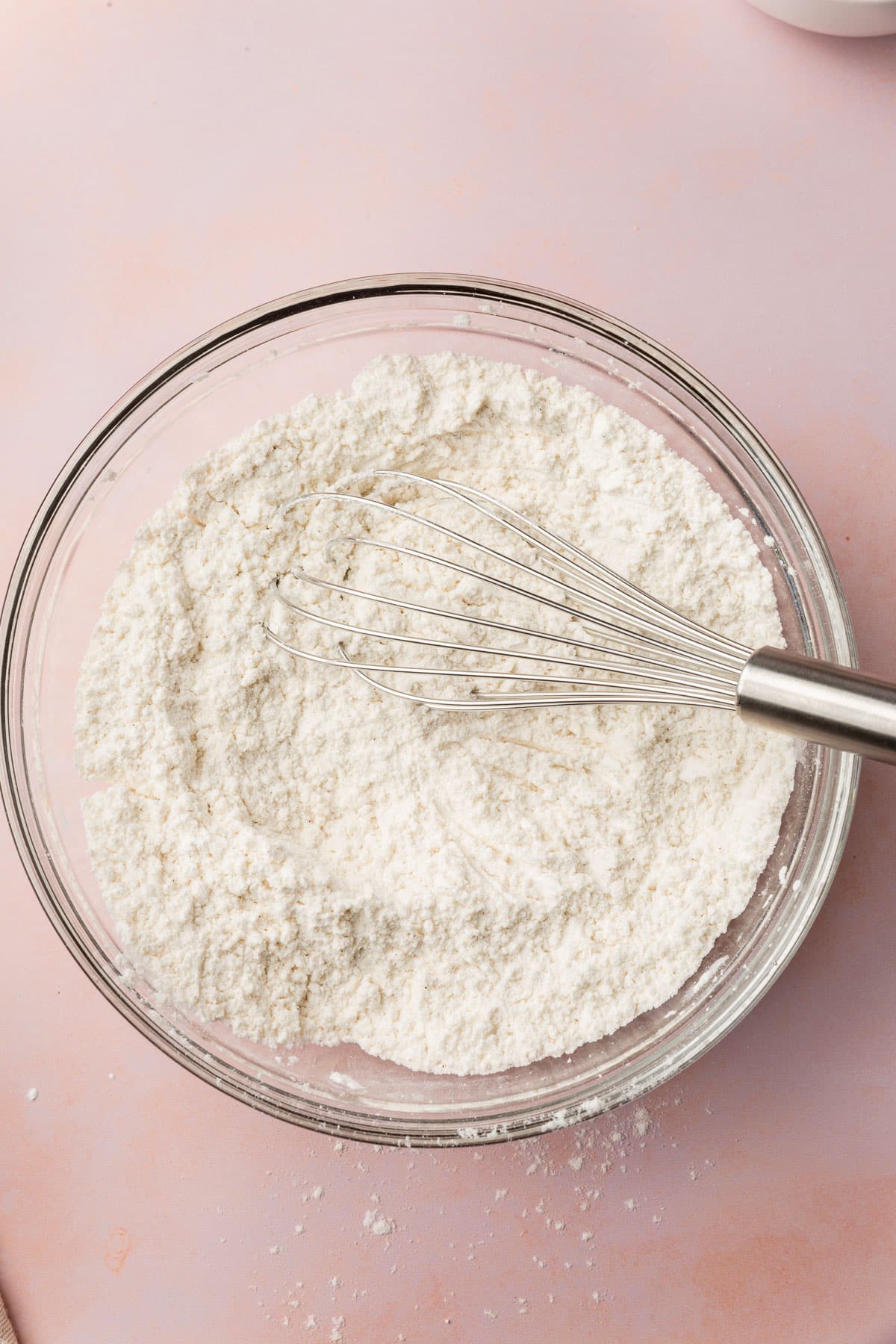 A glass mixing bowl filled with a gluten-free flour blend with a whisk in it.