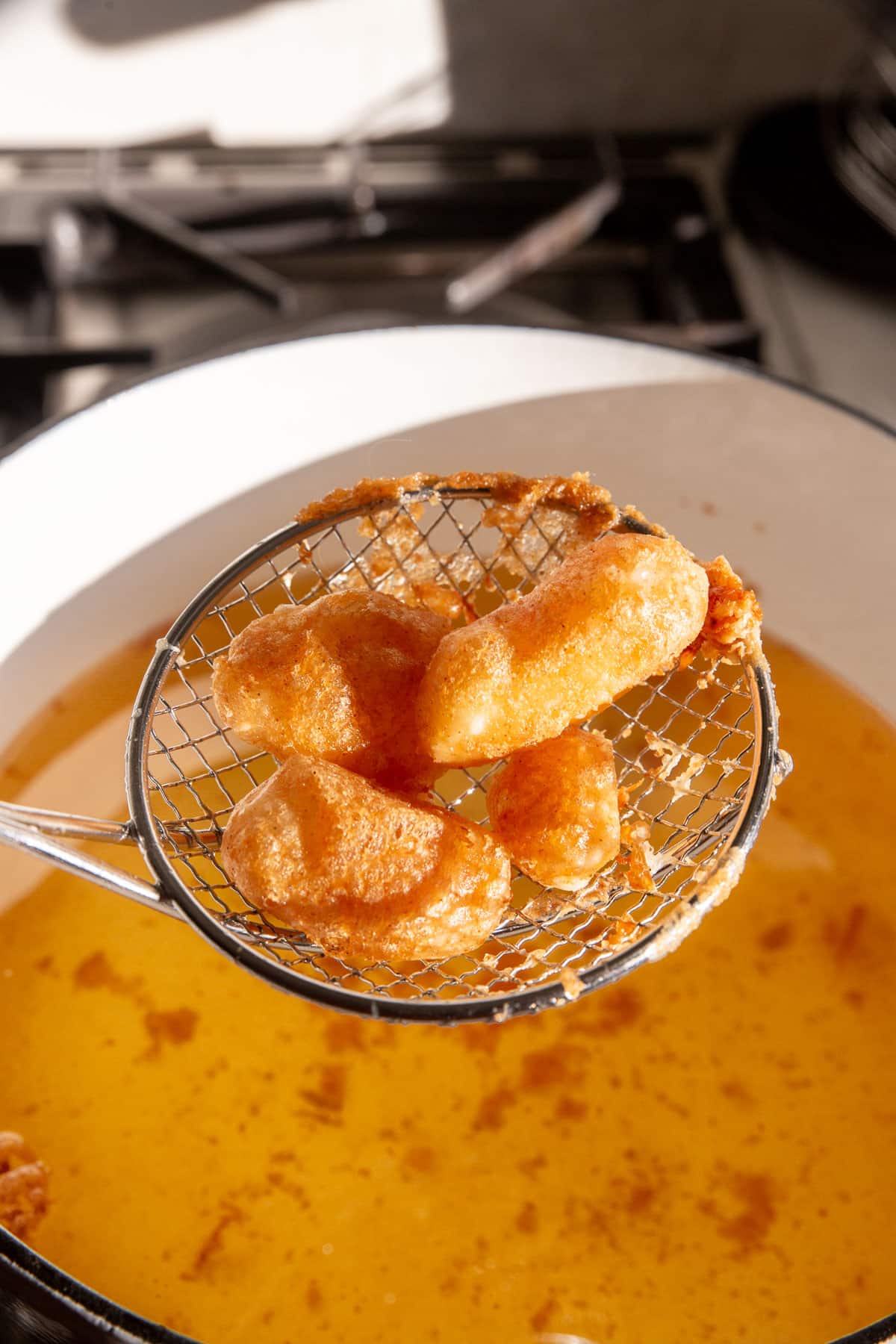 A spider spatula lifting a few gluten-free cheese curds from a pot of hot oil.