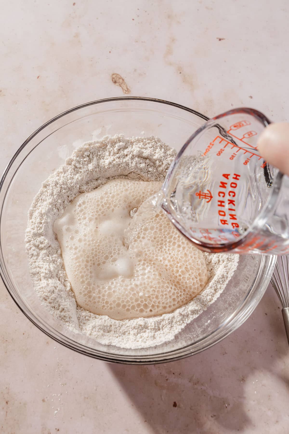 A measuring cup of club soda being poured into gluten-free flour blend and baking soda to make a gluten-free batter.