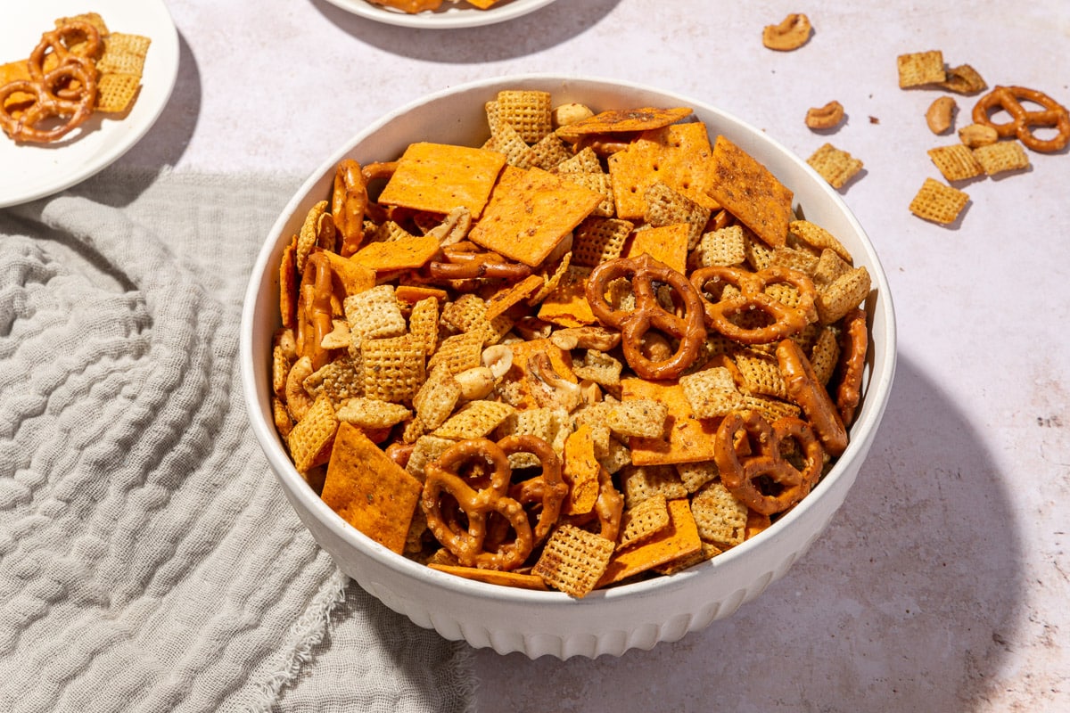 A serving bowl filled with gluten-free chex mx in it with appetizer plates filled with more snack mix to the side.