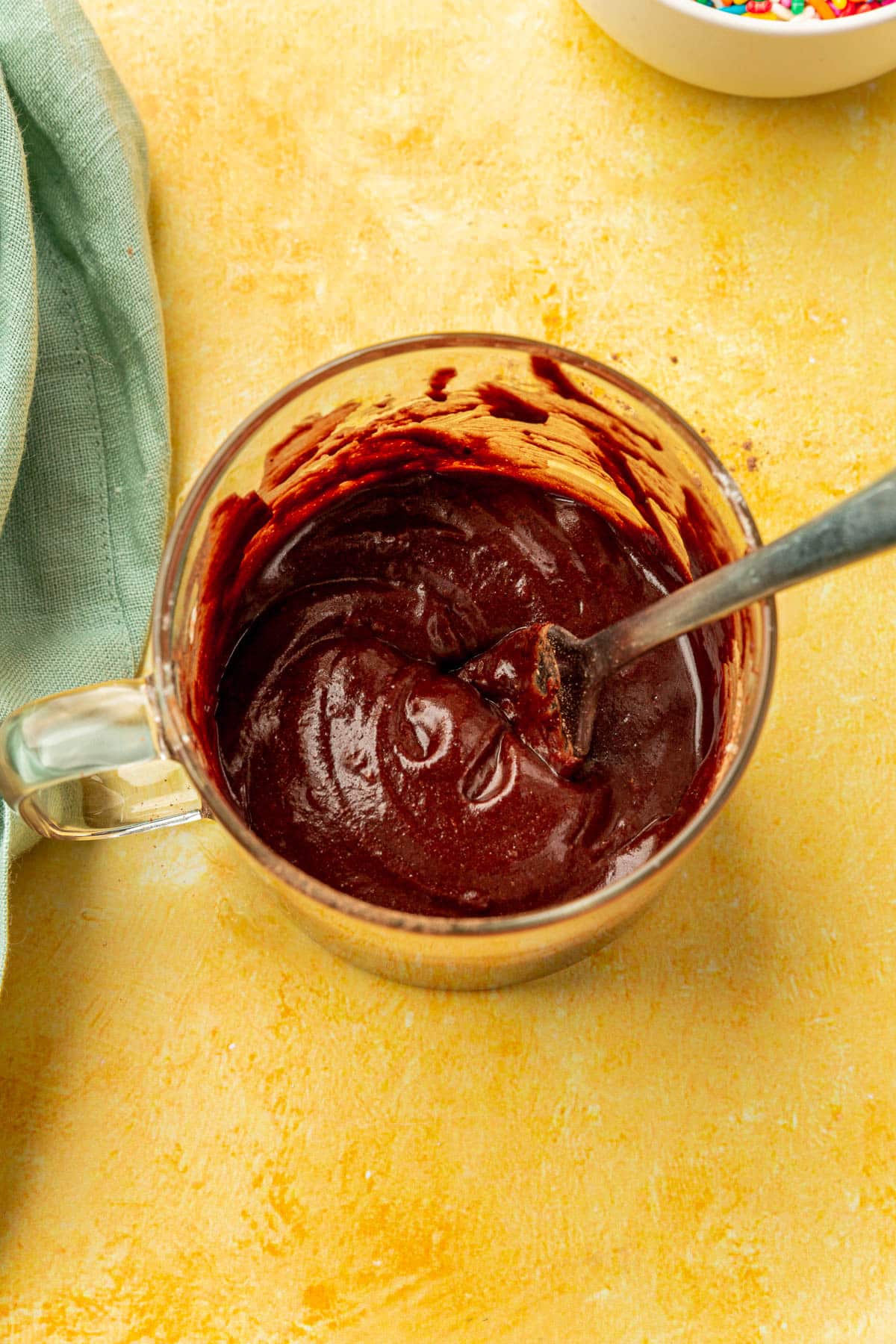 Gluten-free chocolate cake batter in a glass mug being mixed with a fork.