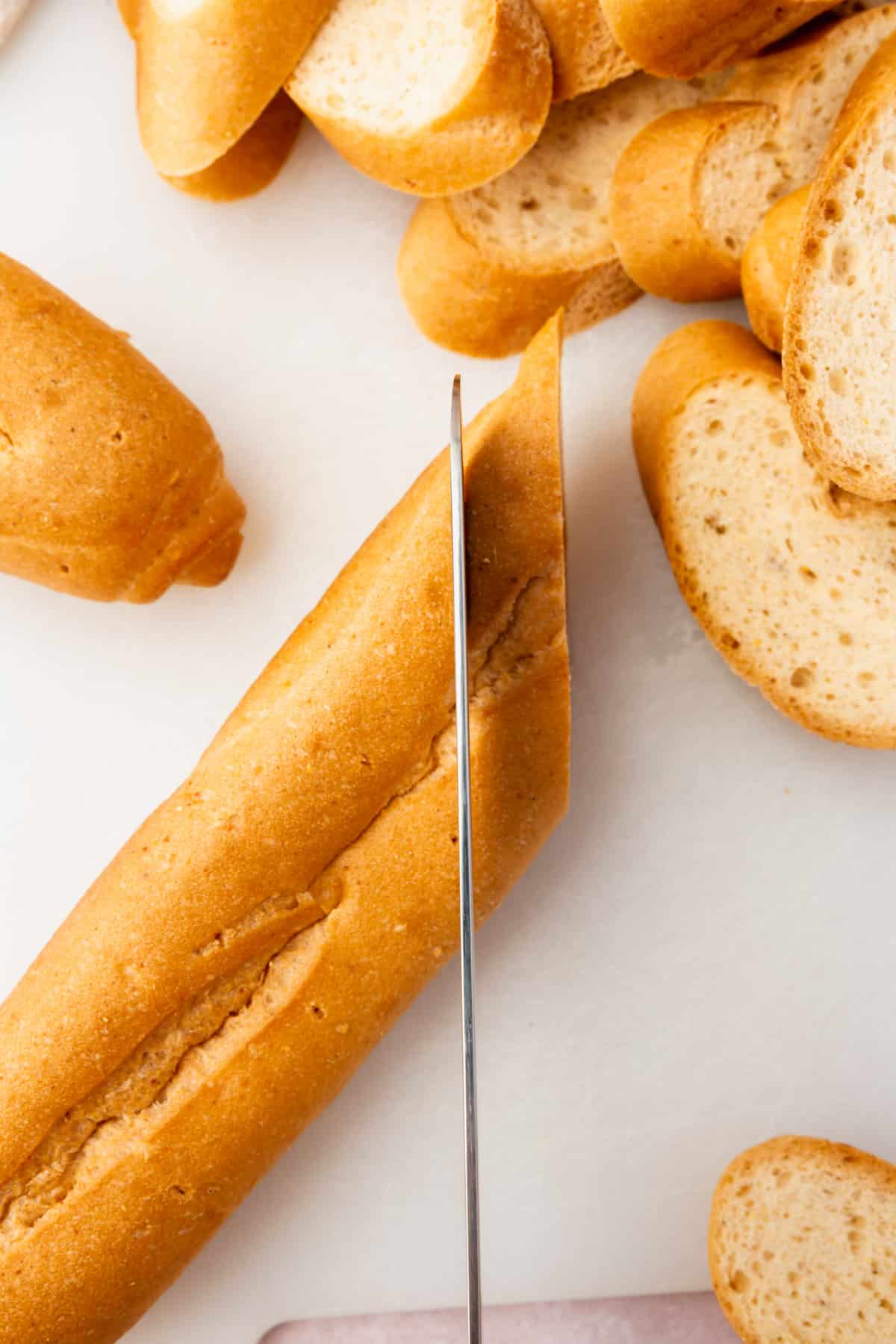 A knife cutting a loaf of gluten free french bread on the bias into slices for bruschetta.