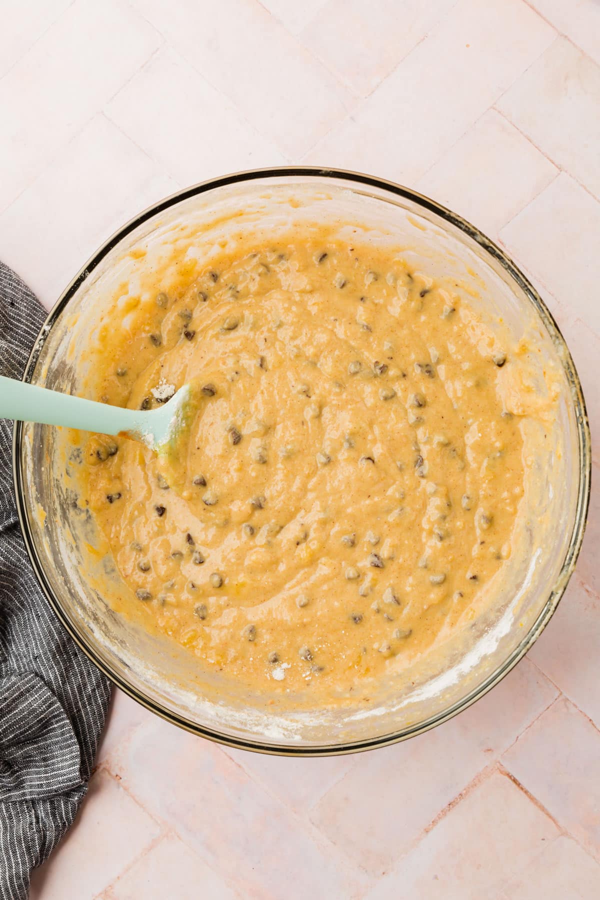 A glass mixing bowl with gluten free banana bread batter with mini chocolate chips and a blue spatula in it.