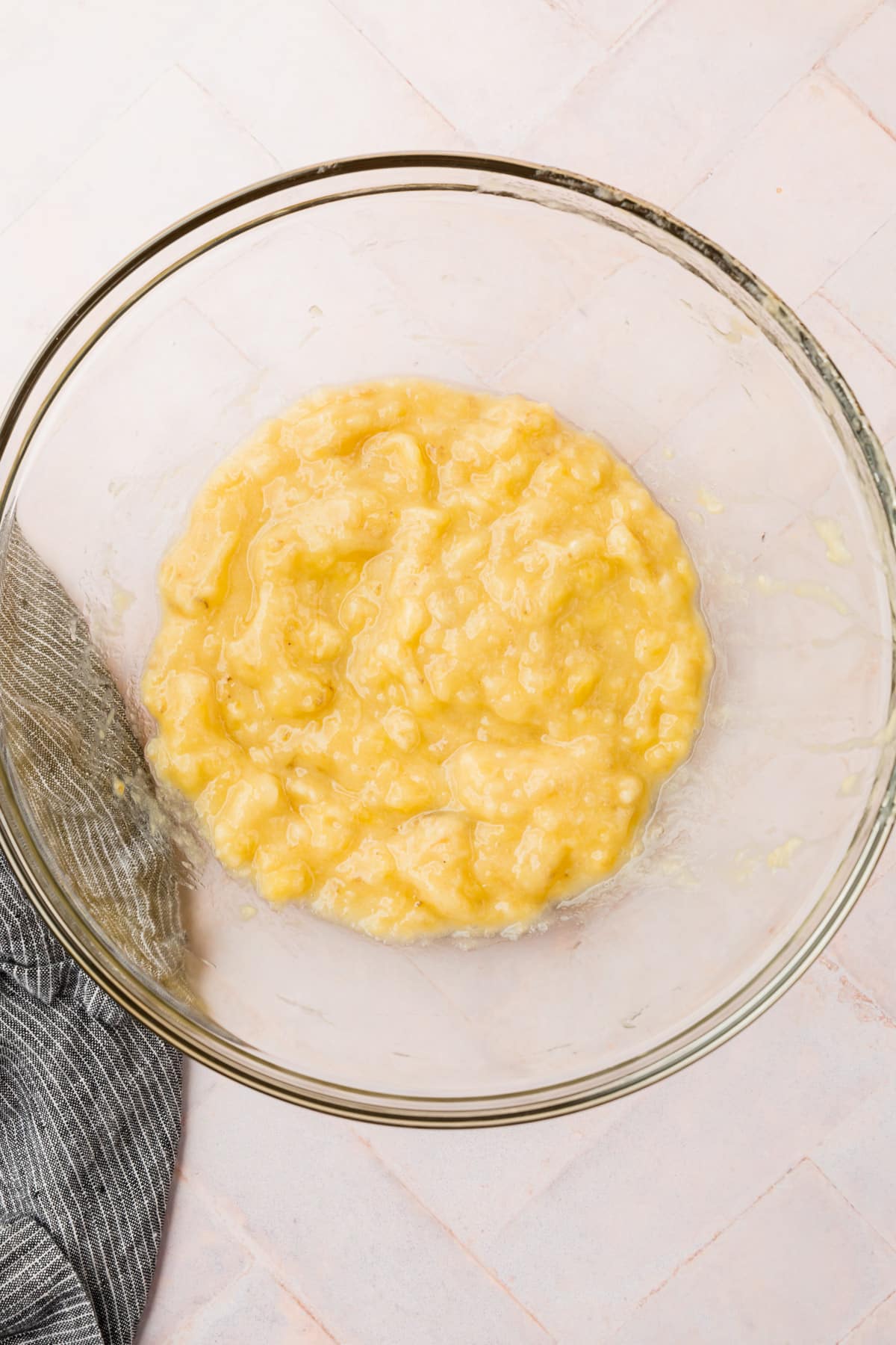 A glass mixing bowl with mashed bananas in it.