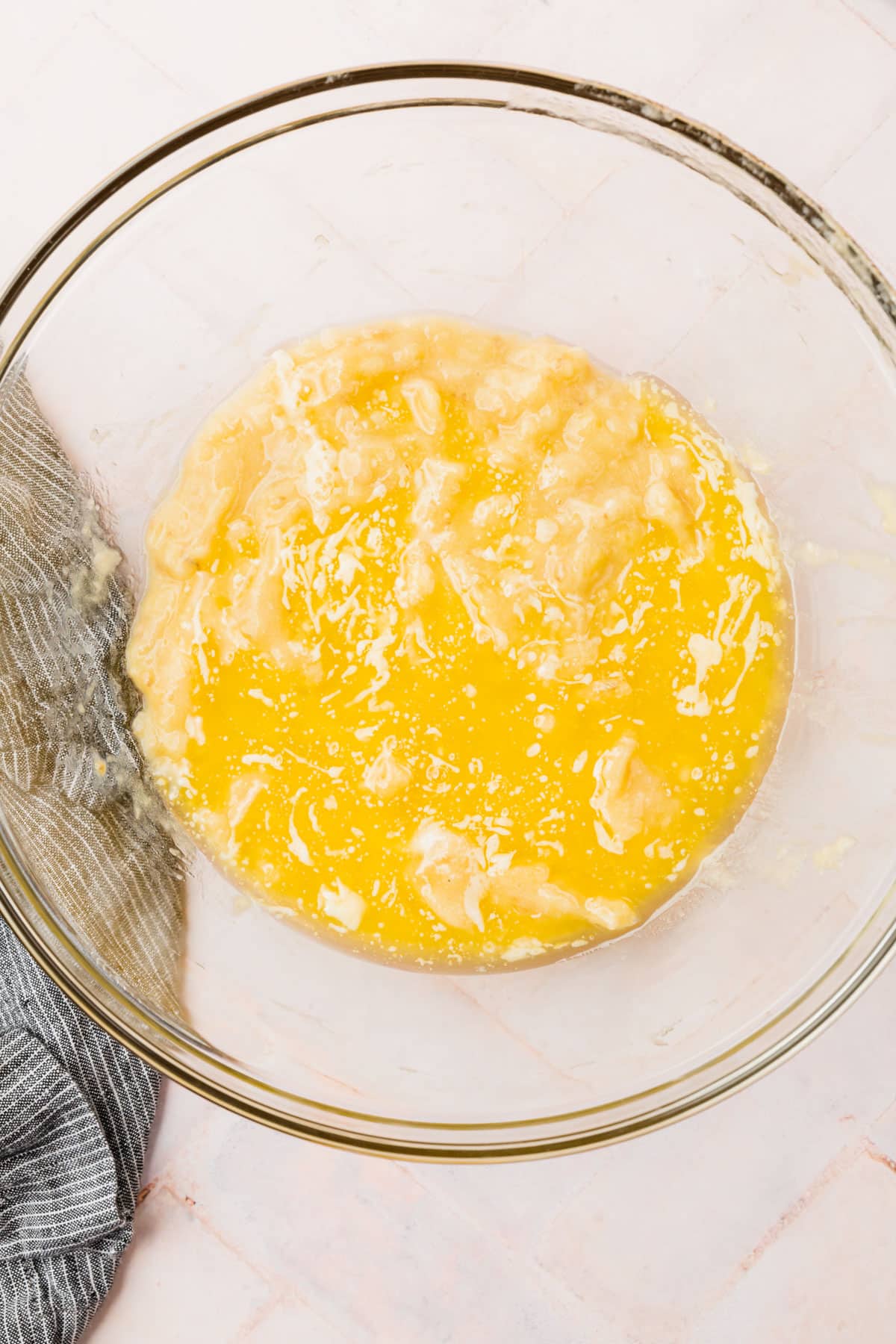 A glass mixing bowl with mashed bananas topped with melted butter before mixing together.
