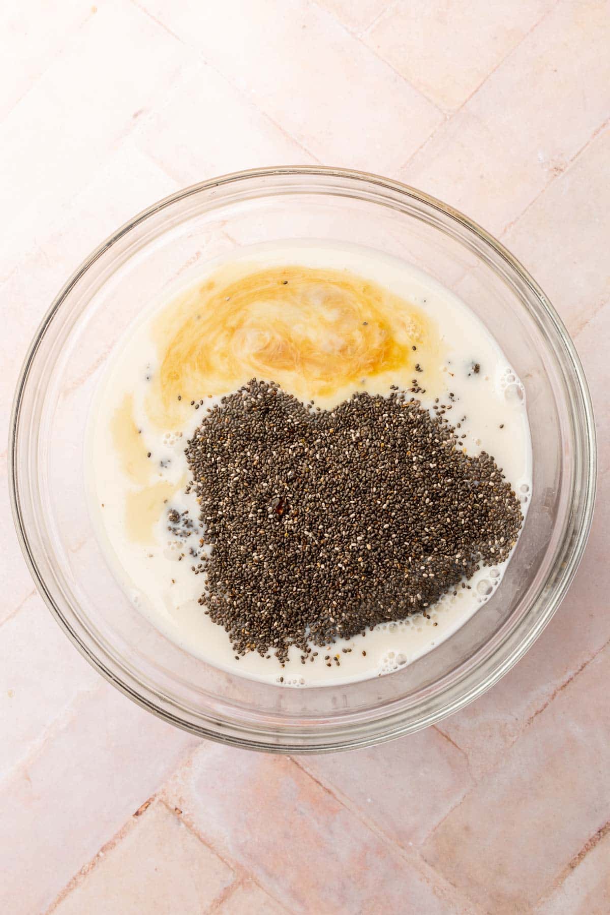 A glass mixing bowl with almond milk, chia seeds, vanilla extract and pure maple syrup before whisking together.