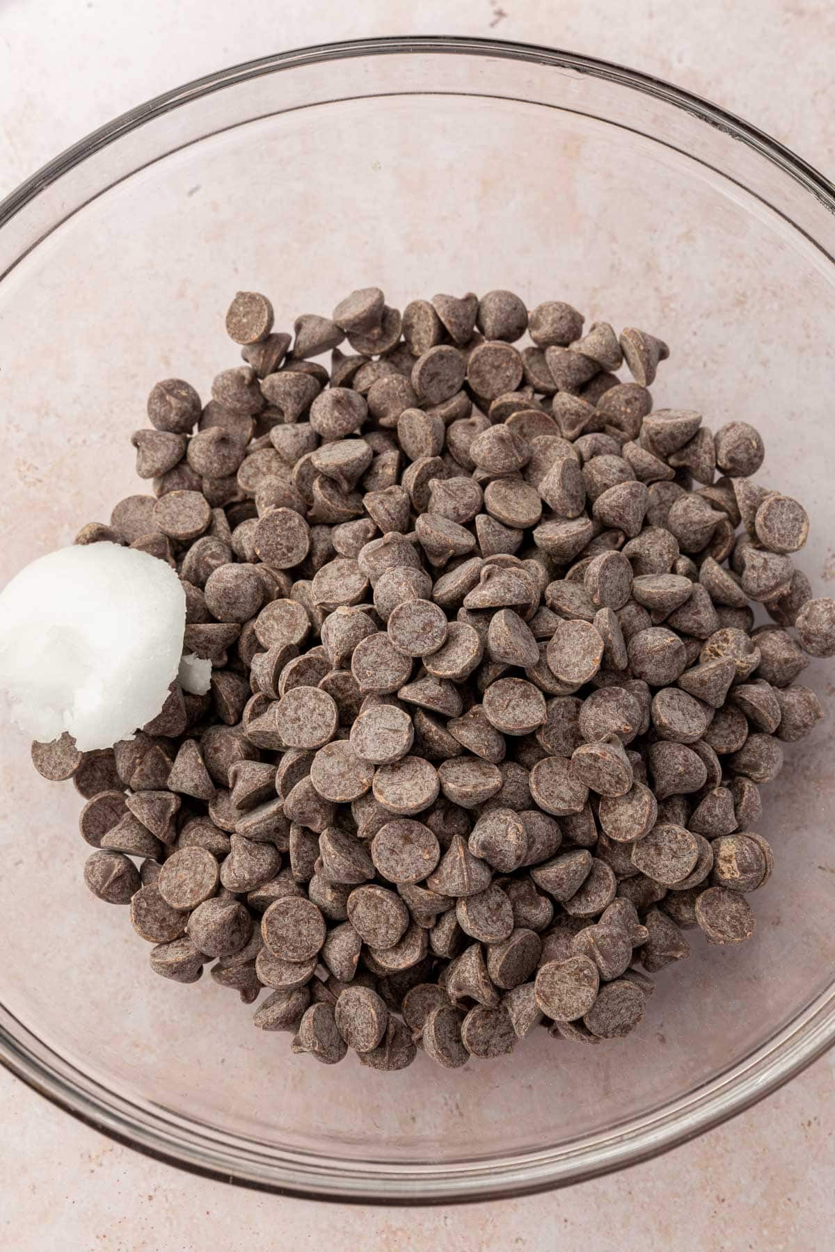 A glass mixing bowl with dark chocolate chips and coconut oil in it before melting in the microwave.
