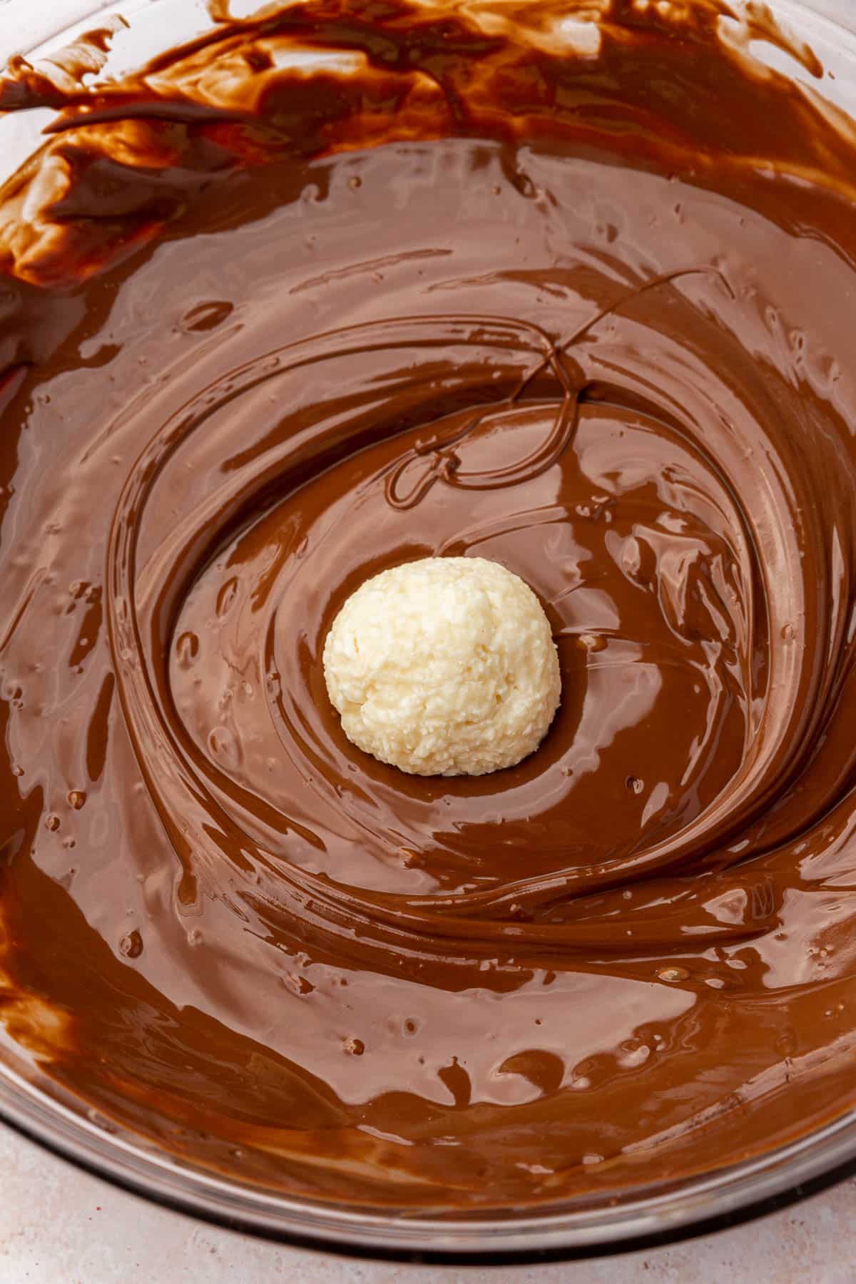 A coconut ball in a bowl of melted dark chocolate.