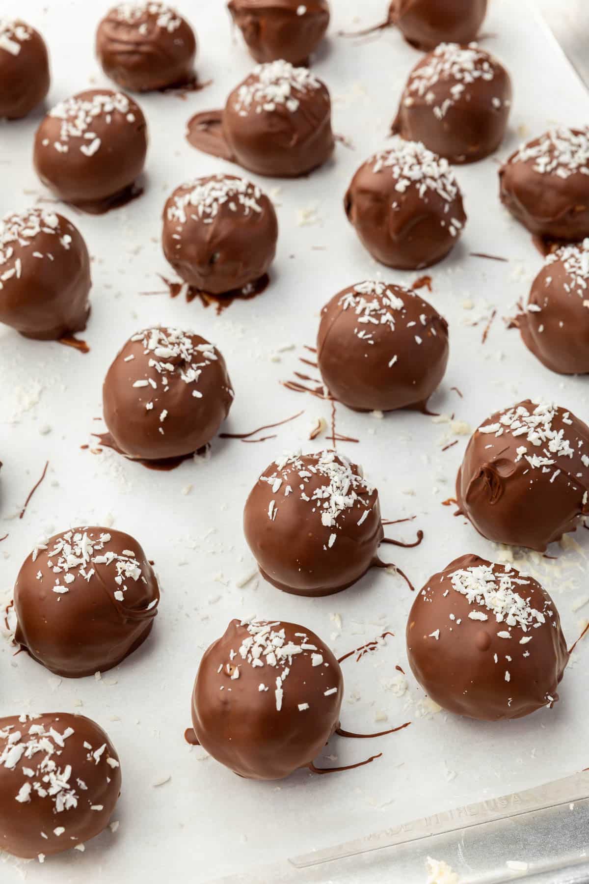Round truffles covered in dark chocolate coating and topped with shredded coconut on a baking sheet lined with parchment paper.