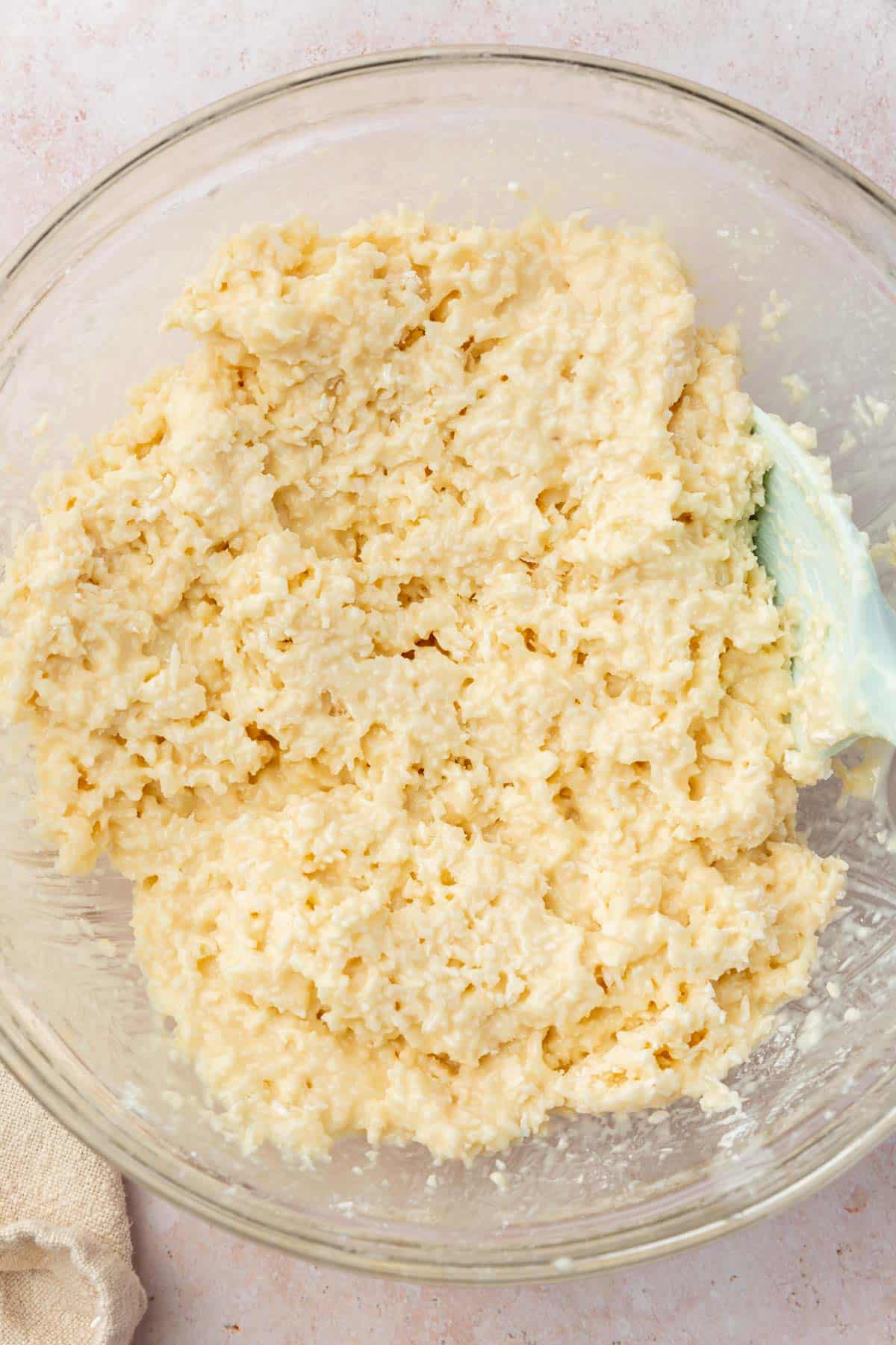 A glass mixing bowl with a coconut truffle dough in it made of coconut flakes and sweetened condensed milk.