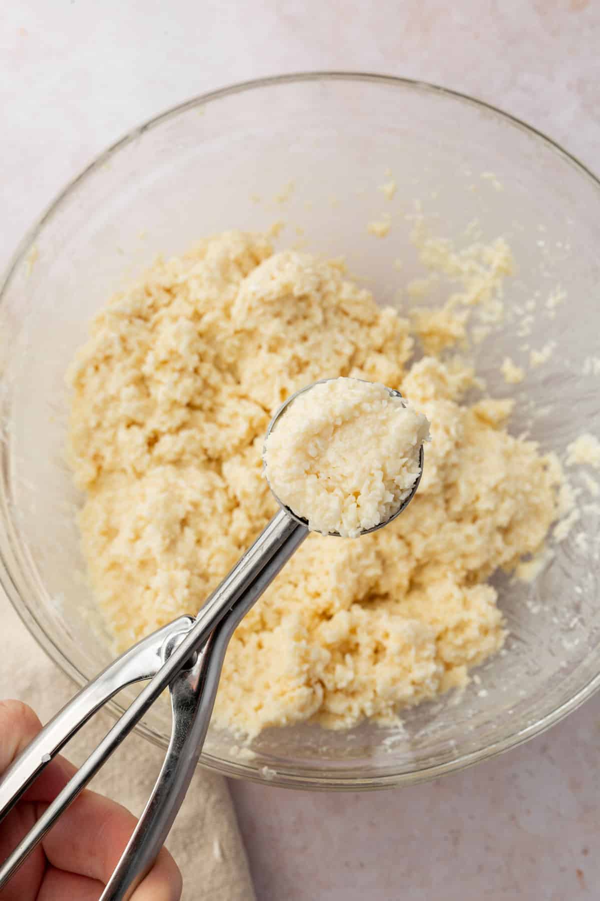 A small stainless steel scooper filled with coconut truffle mixture over a bowl of more coconut truffle dough.