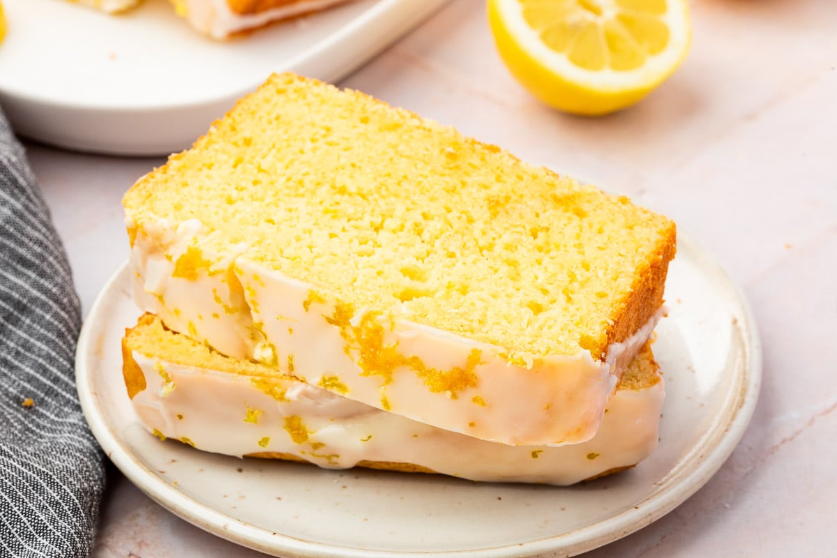 Two slices of gluten-free lemon drizzle cake on a dessert plate with a lemon half in the background.