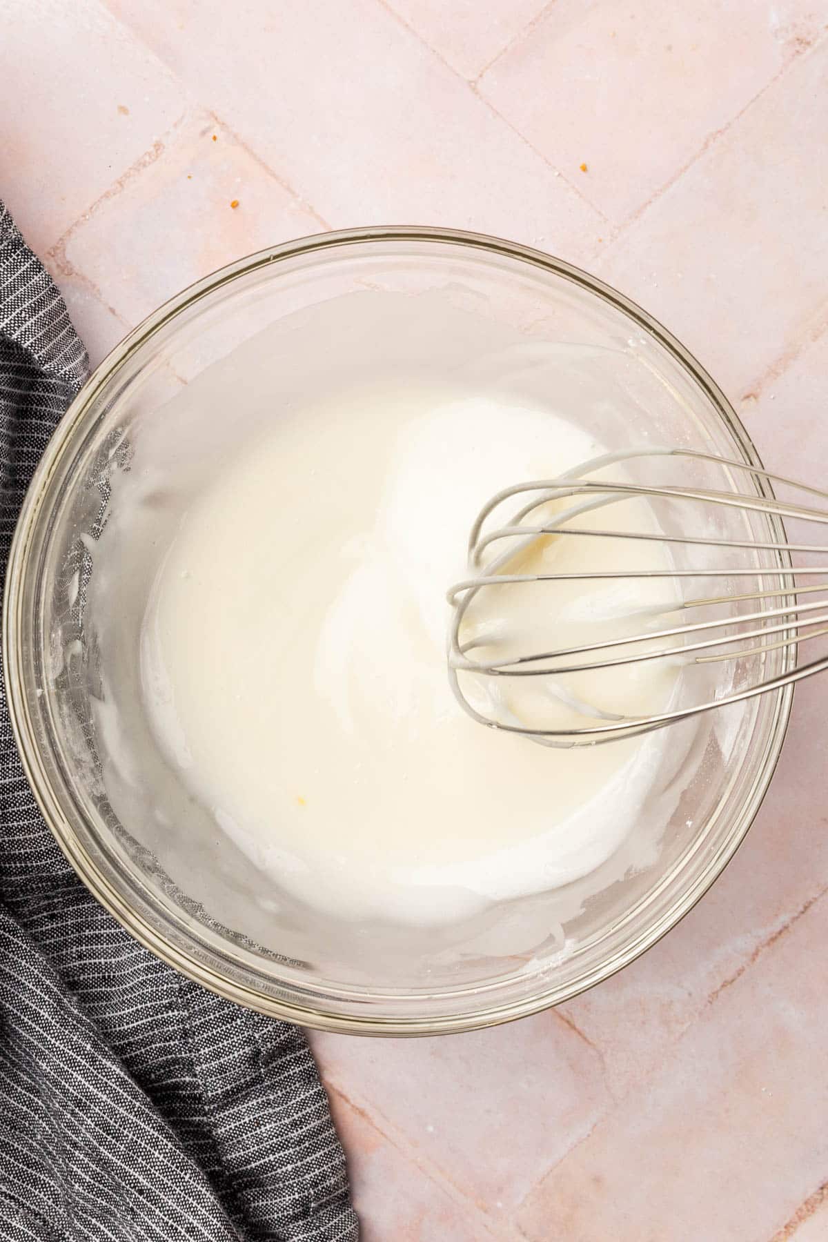 A glass mixing bowl with a lemon glaze and a whisk.
