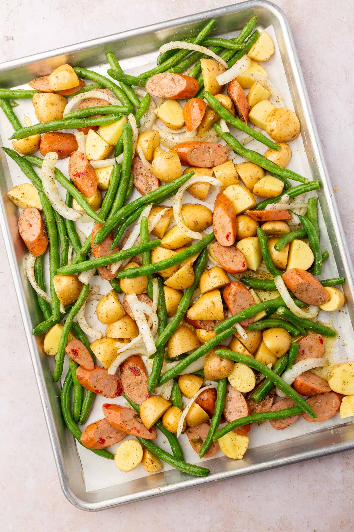 A sheet pan filled with onions, green beans, potatoes and sausage before baking in the oven.