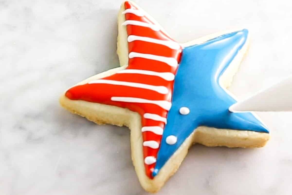 A piping bag of white royal icing piping dots onto a star shaped sugar cookie for 4th of july.