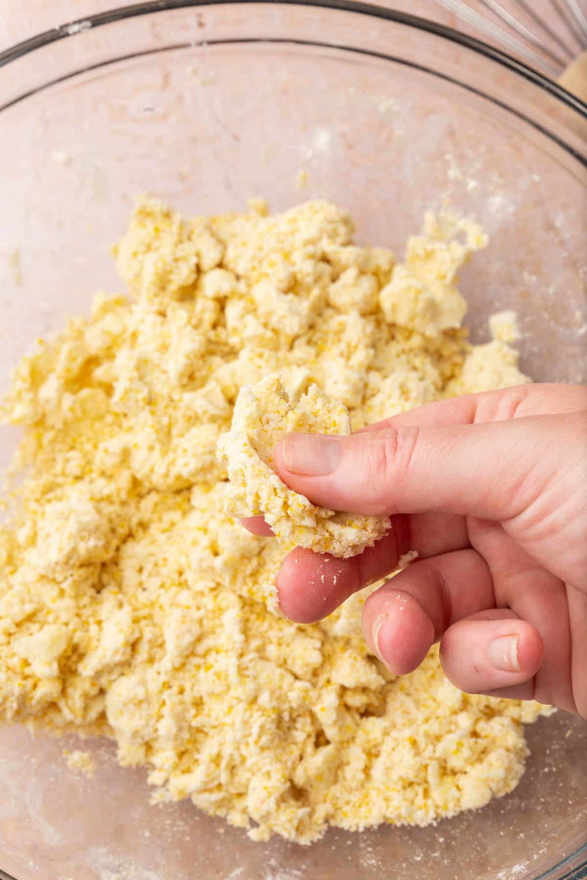 A hand pinching a piece of gluten-free tart dough over a bowl of more dough.