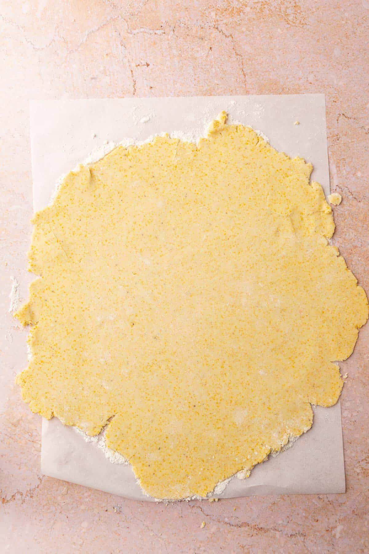 A piece of gluten-free tart dough that has been rolled out into a circle on a piece of floured parchment paper.