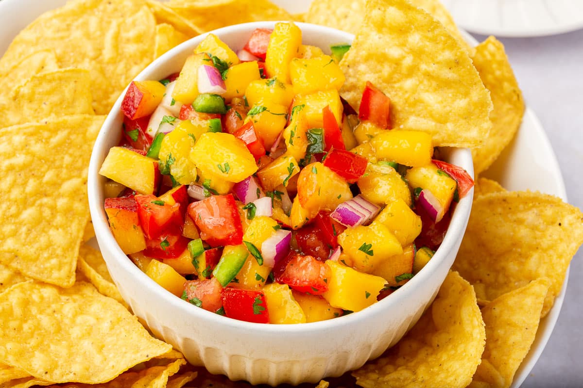 A bowl of peach mango salsa on top of a plate of tortilla chips.
