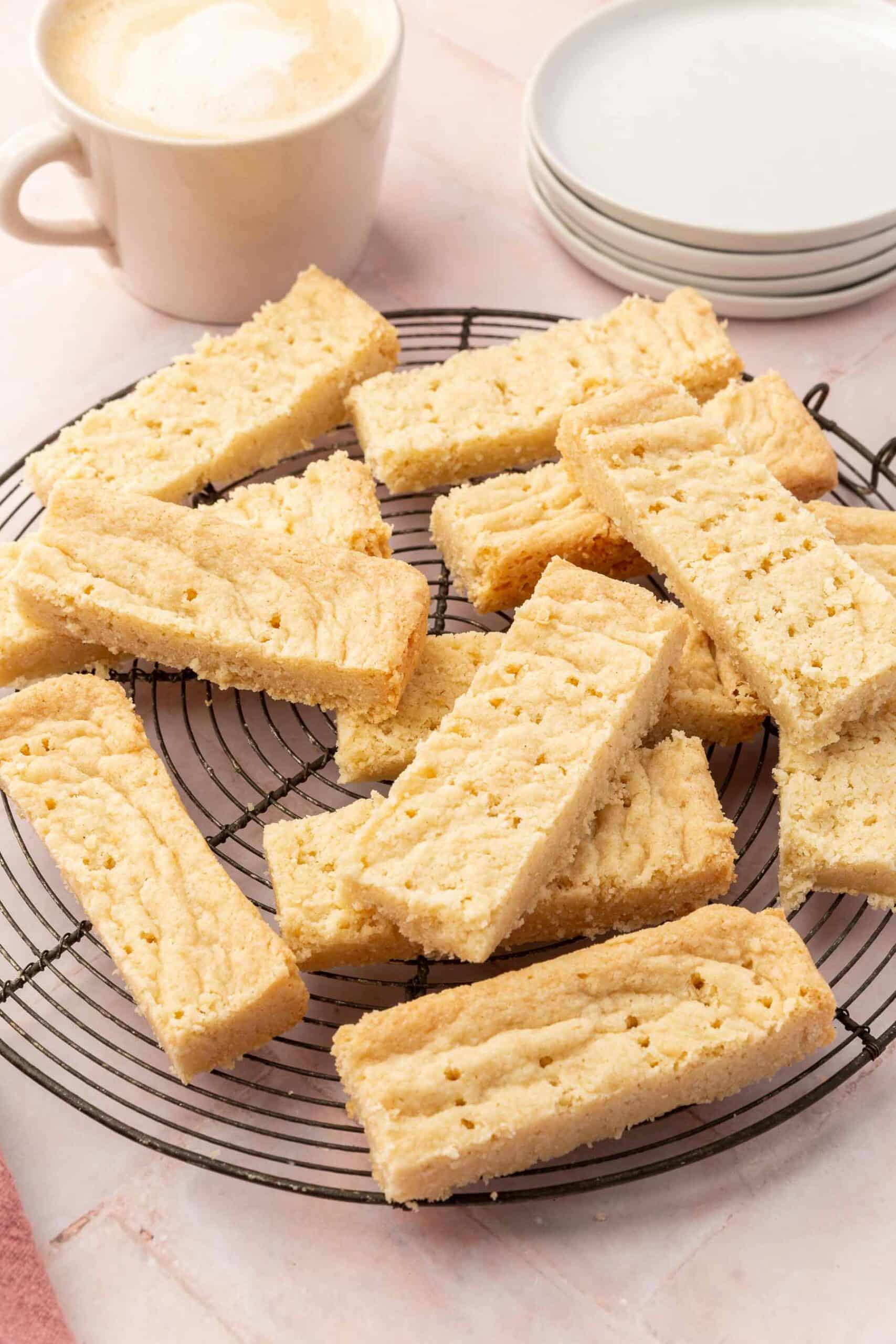 Gluten-free shortbread stacked on top of each other on a round wire cooling rack with a latte and dessert plates in the background.
