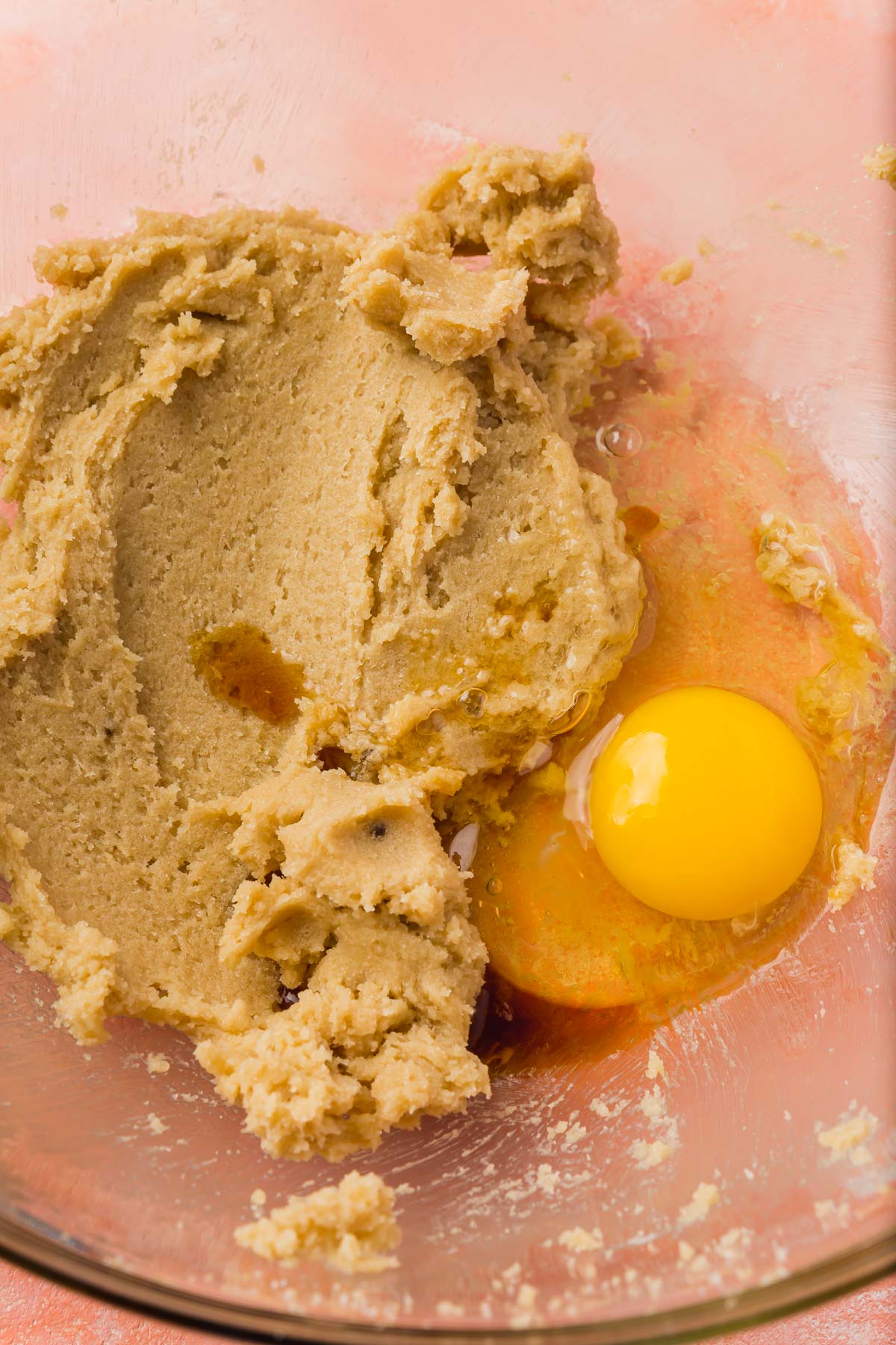 A glass mixing bowl with creamed butter and brown sugar topped with an egg and vanilla extract.