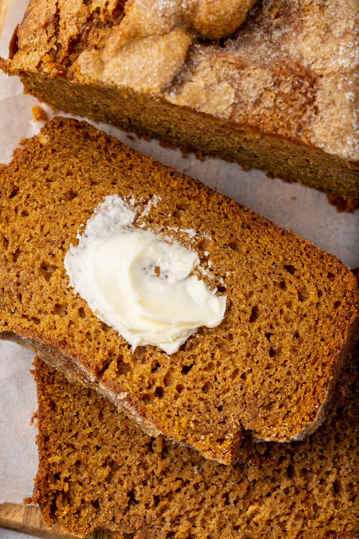 A close up of two slices of gluten free pumpkin bread sliced off from the larger loaf and slathered with butter.