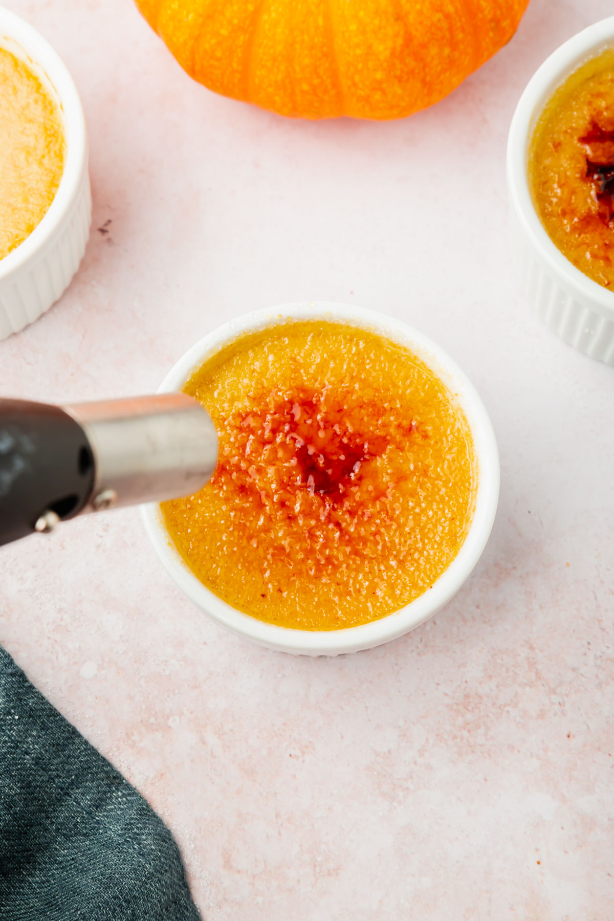 A kitchen torch caramelizing granulated sugar on top of pumpkin crème brûlée in a ramekin.