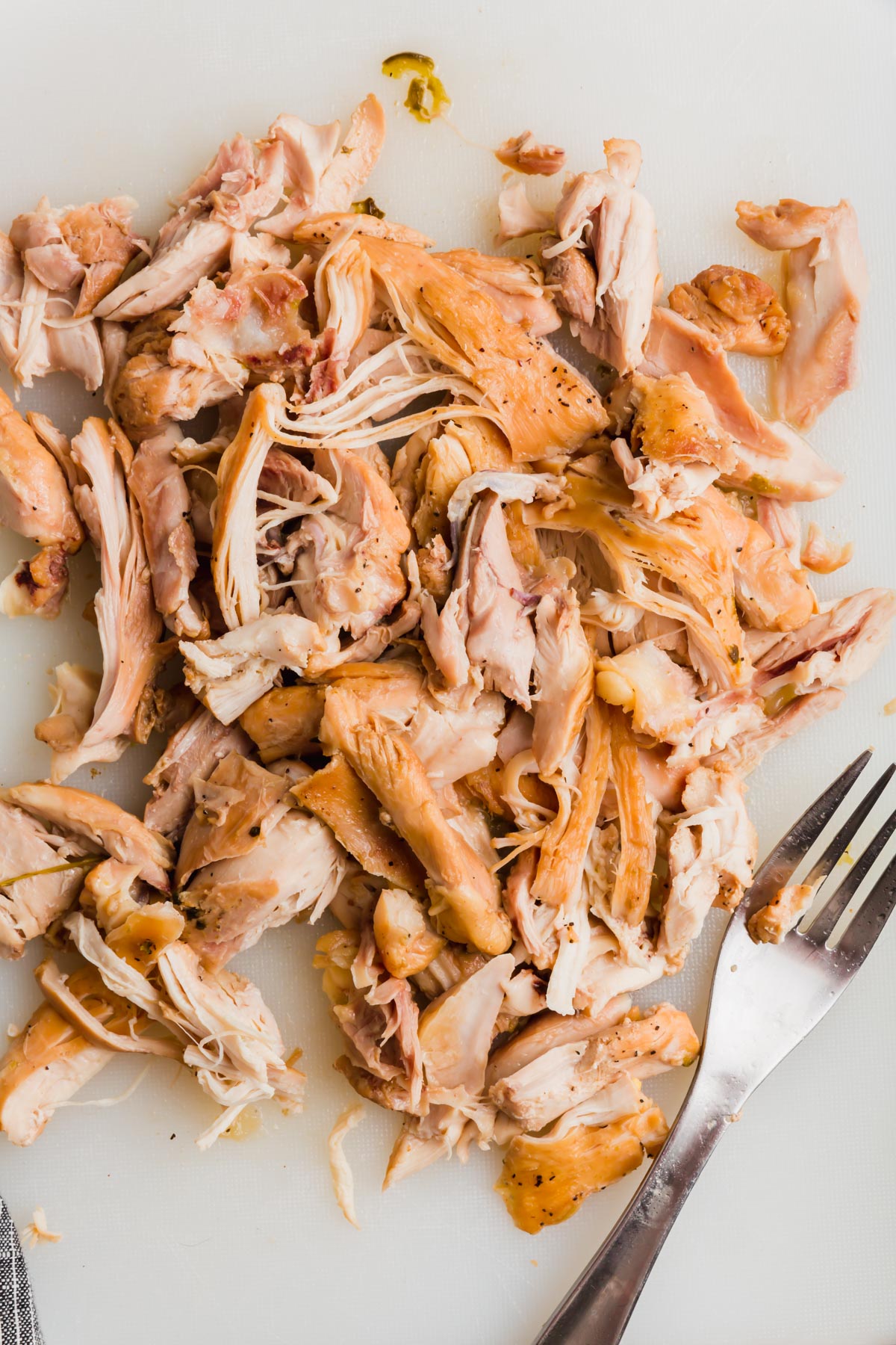 Shredded chicken thighs on a white cutting board with a fork.