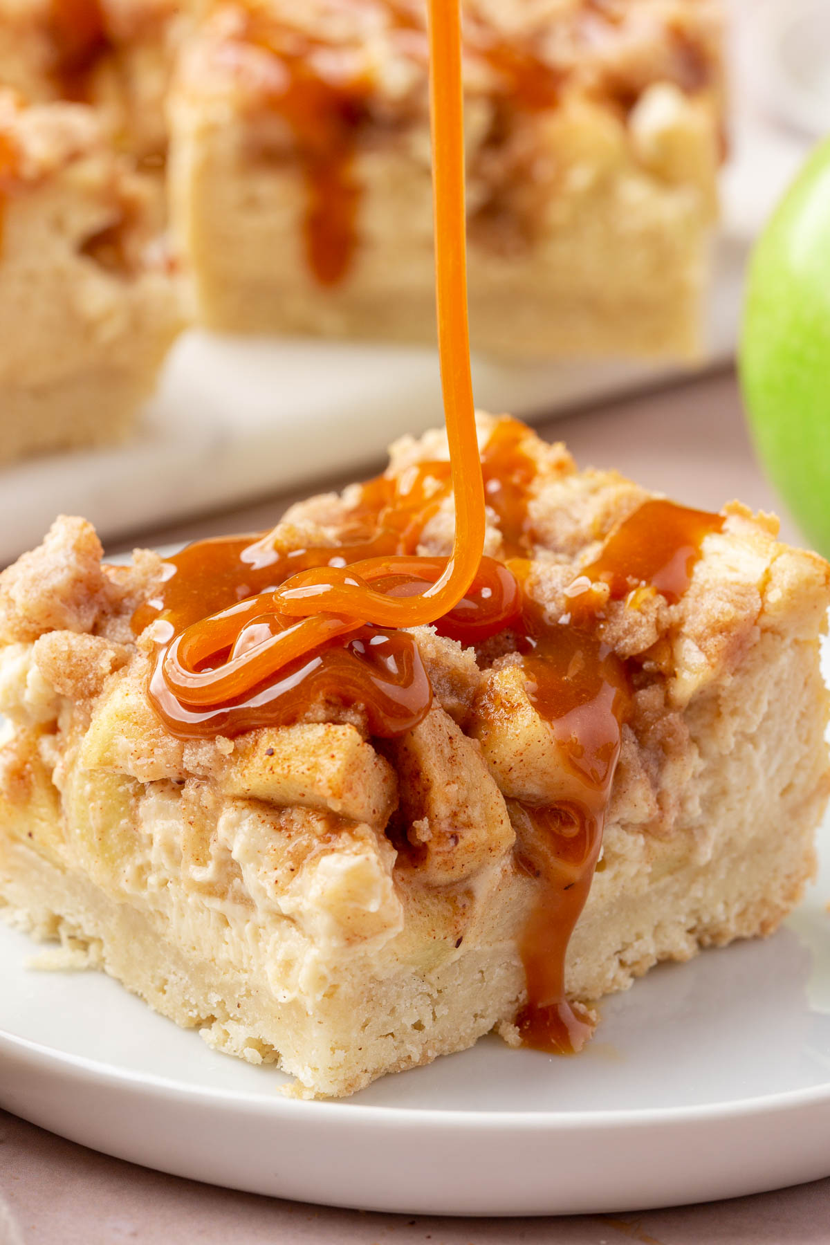 A stream of caramel sauce being drizzled over a gf apple caramel cheesecake bar on a dessert plate.