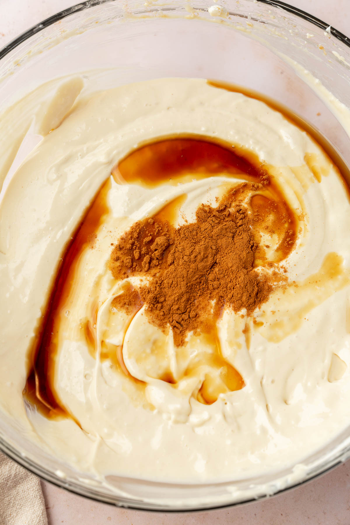 A glass mixing bowl with a cheesecake filling topped with vanilla extract and ground cinnamon.