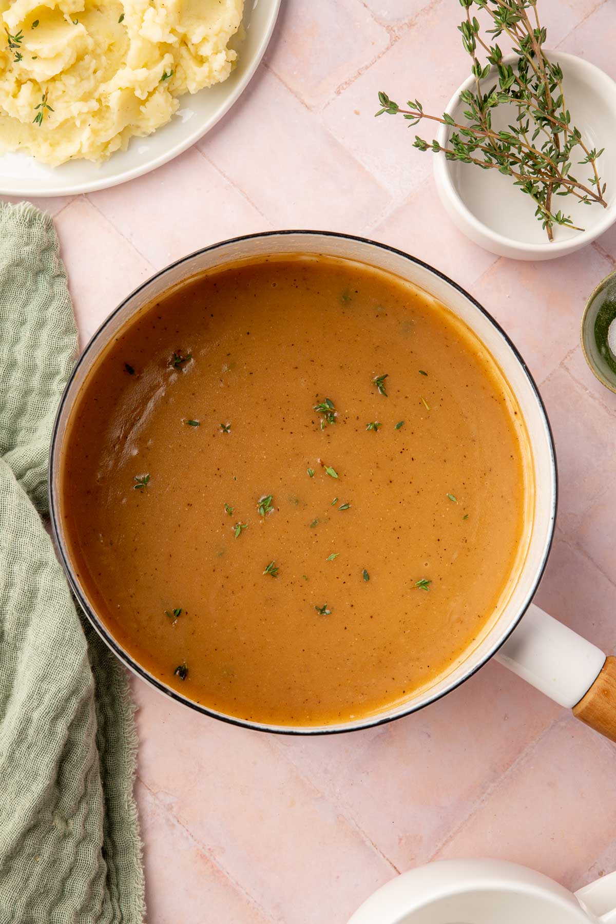 An overhead view of a white saucepan filled with gluten-free gravy topped with fresh thyme.