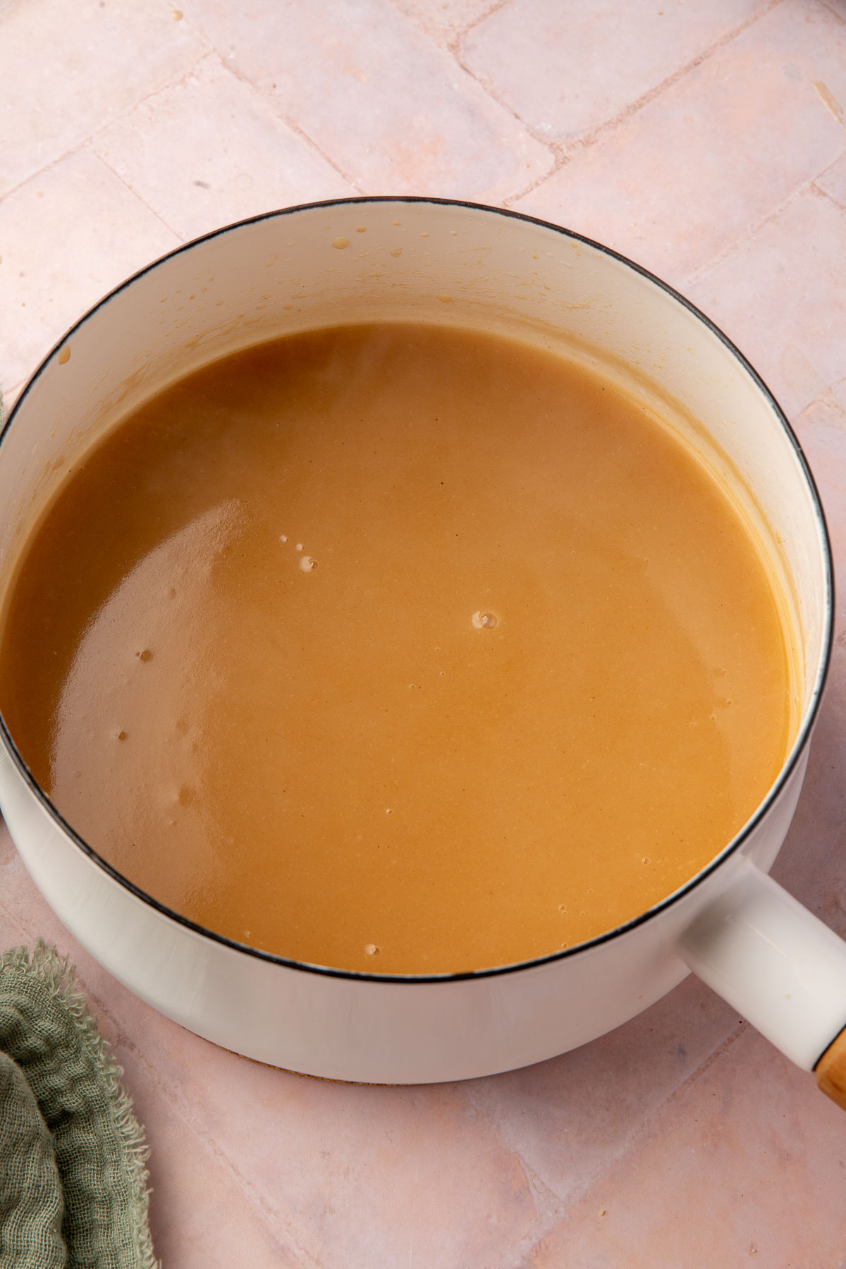 A white saucepan of gluten-free gravy on a pink table.