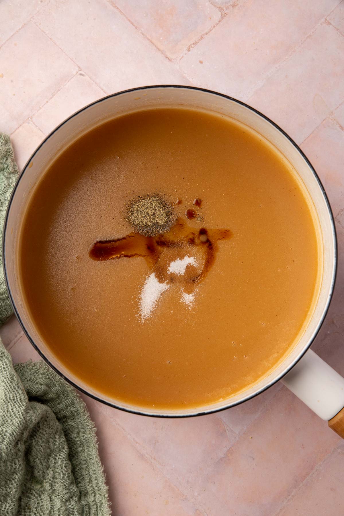 A white saucepan with gluten-free gravy topped with salt, pepper and worcestershire sauce in it.