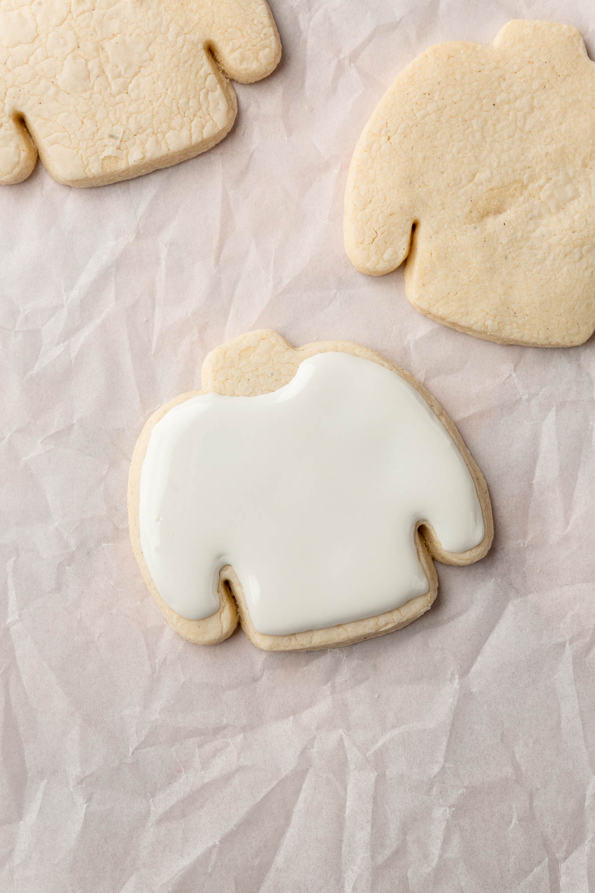 A few gluten free ugly sweater Christmas cookies on a piece of parchment paper with one decorated with white royal icing.