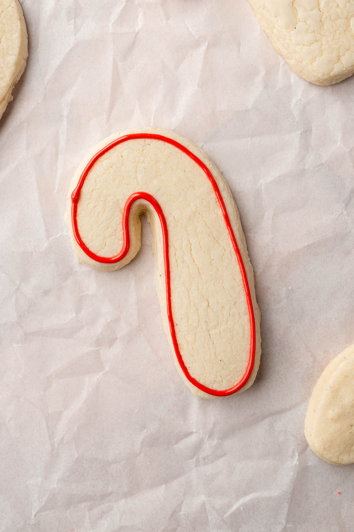 A few gluten free candy cane sugar cookies on a piece of parchment paper with one outlined in red royal icing.