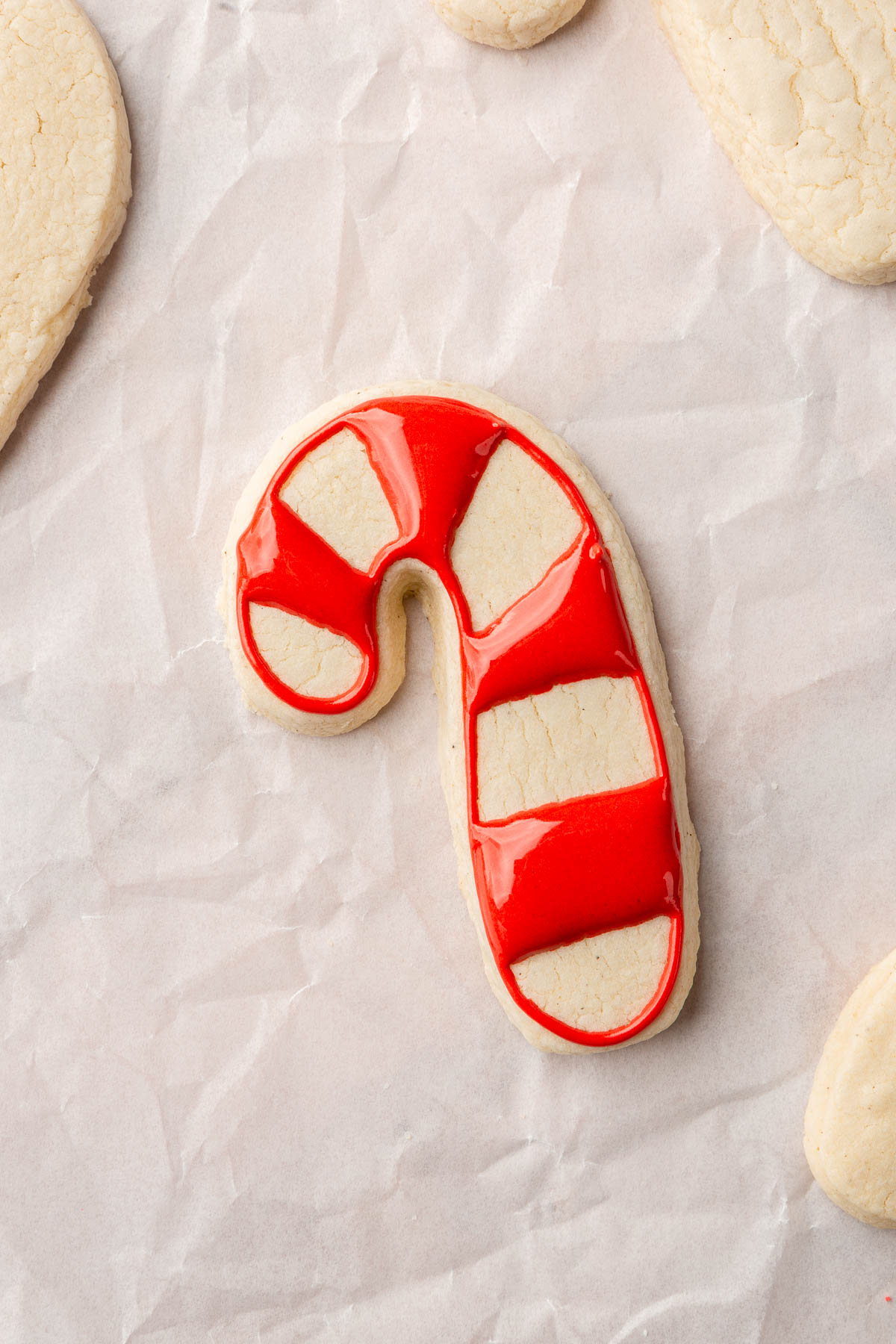 A few gluten free candy cane sugar cookies on a piece of parchment paper with one decorated with red royal icing stripes.