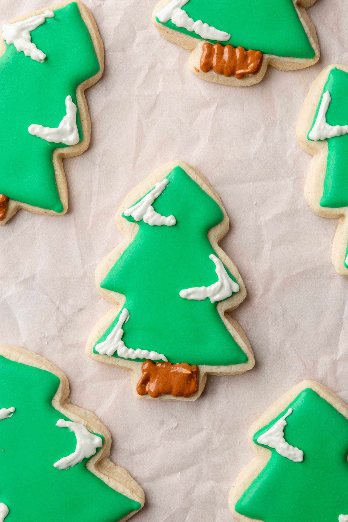 A gluten-free Christmas tree sugar cookie decorated with green royal icing and brown royal icing to create a tree stump with white royal icing to create snow caps on the tree limbs..