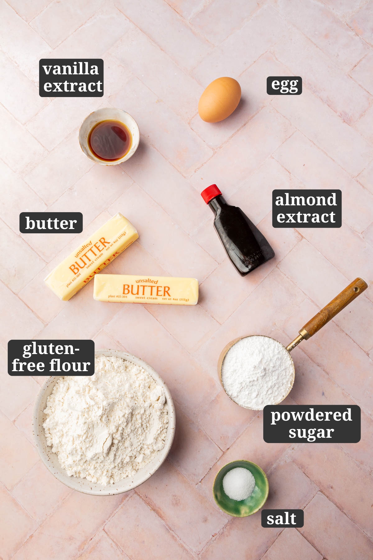 Ingredients in small bowls to make gluten-free sugar cookies, including vanilla extract, egg, almond extract, butter, gluten-free flour, powdered sugar, and salt, with text overlays over each ingredient.