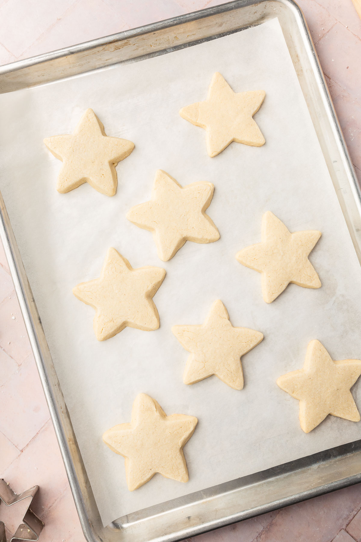 Star shaped gluten free sugar cookies on a baking sheet lined with parchment paper after baking in oven.