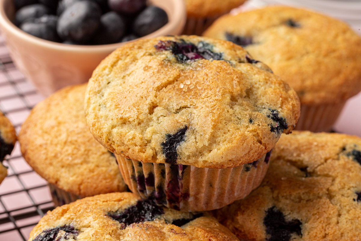 A stack of gluten free blueberry muffins on a wire cooling rack with a small bowl of fresh blueberries in the background.
