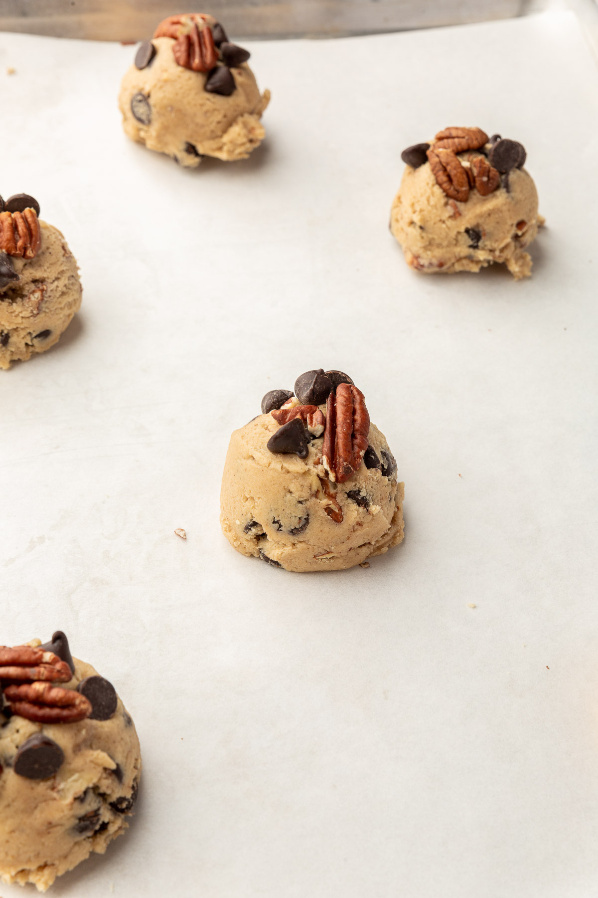 A close up of gluten-free pecan chocolate chip cookie dough balls on a baking sheet lined with parchment paper before baking in the oven.