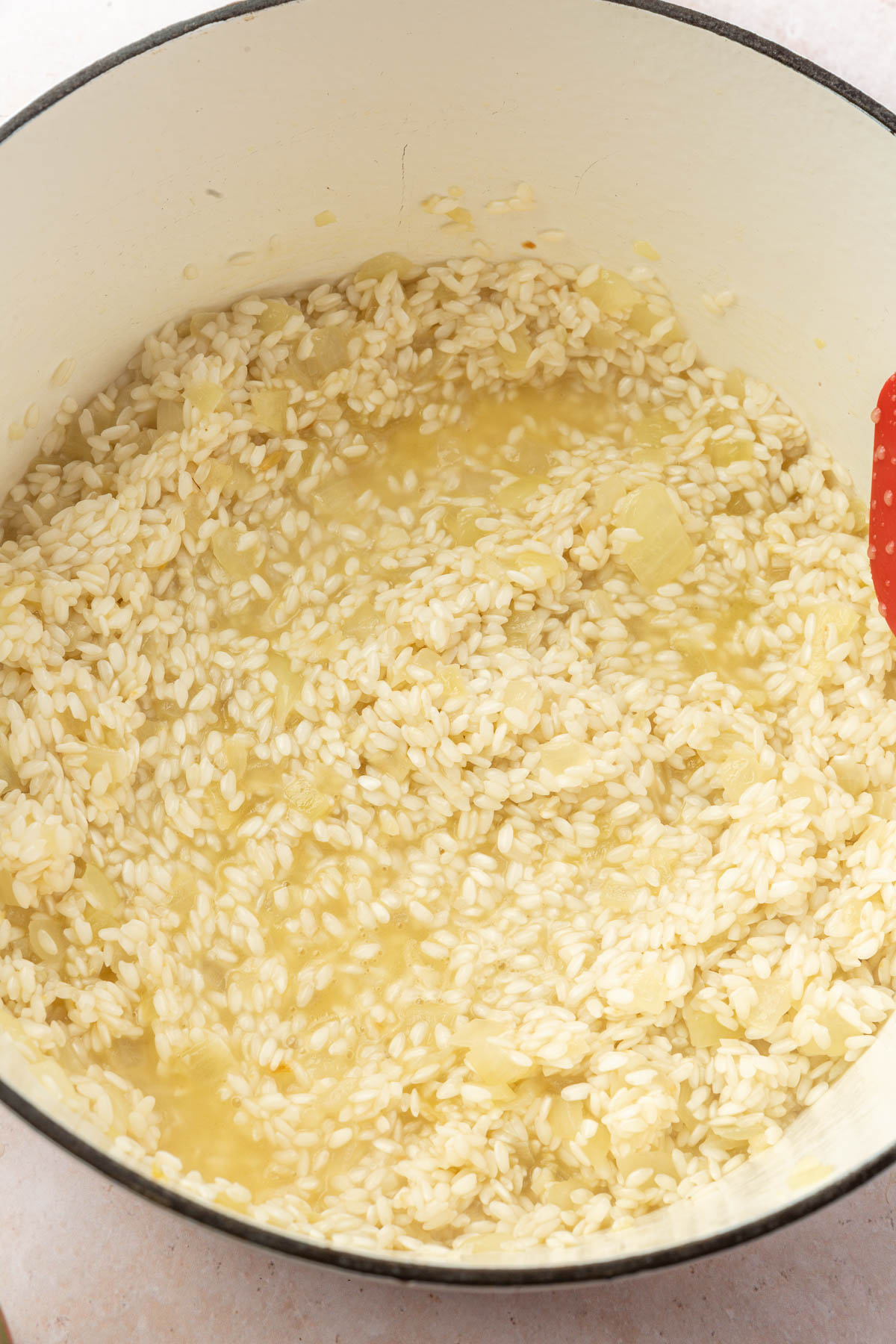 Risotto being cooked in a white dutch oven with chicken broth.