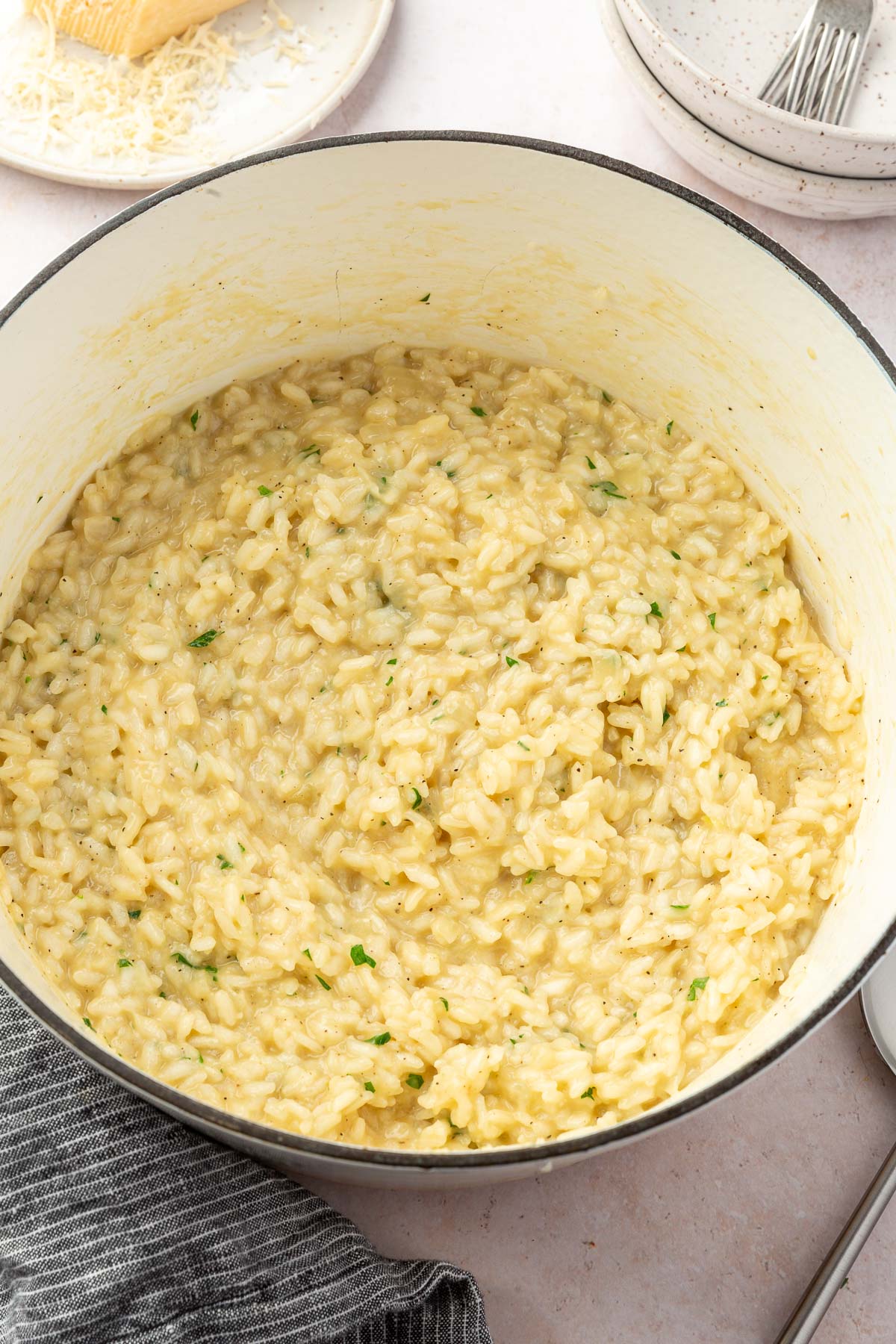 A white dutch oven with parmesan risotto mixed with parsley.